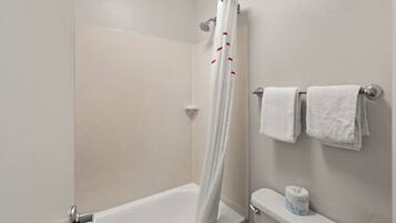 A bathroom with a shower curtain, a toilet, and a stack of white towels.