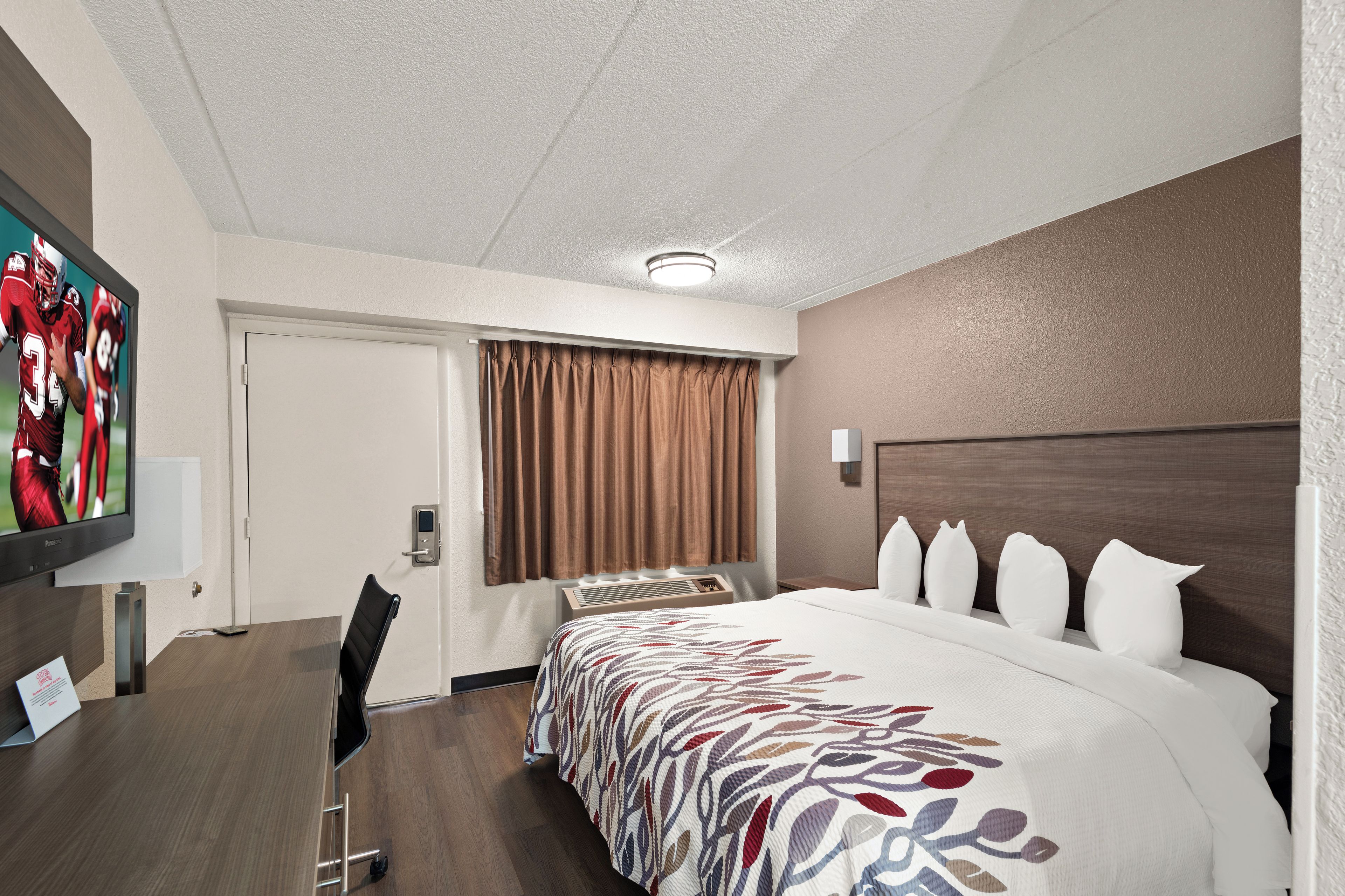 A hotel room with a large bed, a desk with a chair, a television, and a window with curtains.
