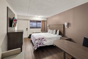 Une chambre d’hôtel comprenant un lit, une table de chevet, un bureau, une chaise, un téléviseur fixé au mur et une fenêtre avec des rideaux.