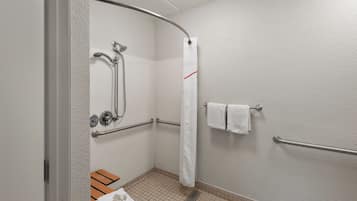 Un baño con ducha, barras de apoyo, toallero y un banco.