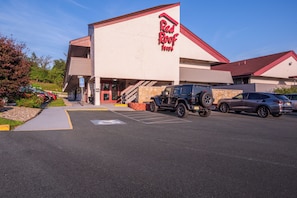 Een Red Roof Inn met een zichtbaar parkeerplaatsbord voor gehandicapten, een overdekt buitengebied en een parkeerplaats met voertuigen.