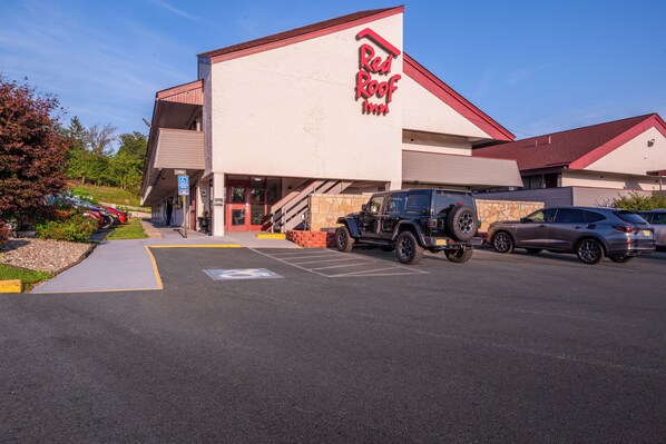 Un hotel Red Roof Inn con señalización visible para estacionamiento de discapacitados, un área exterior cubierta y un estacionamiento con vehículos.