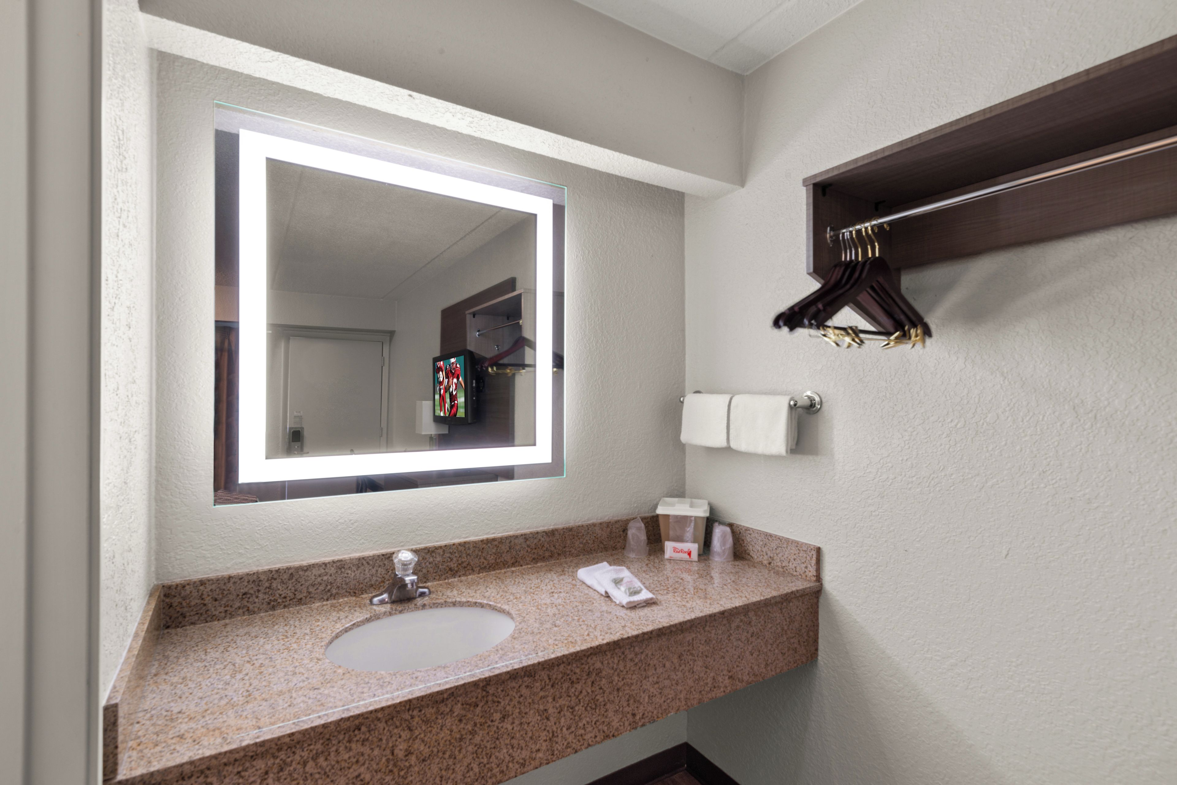 A bathroom with a sink, mirror, towel rack, and a towel dispenser.