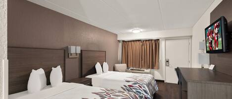 Habitación de hotel con dos camas, un escritorio, un televisor y una puerta.