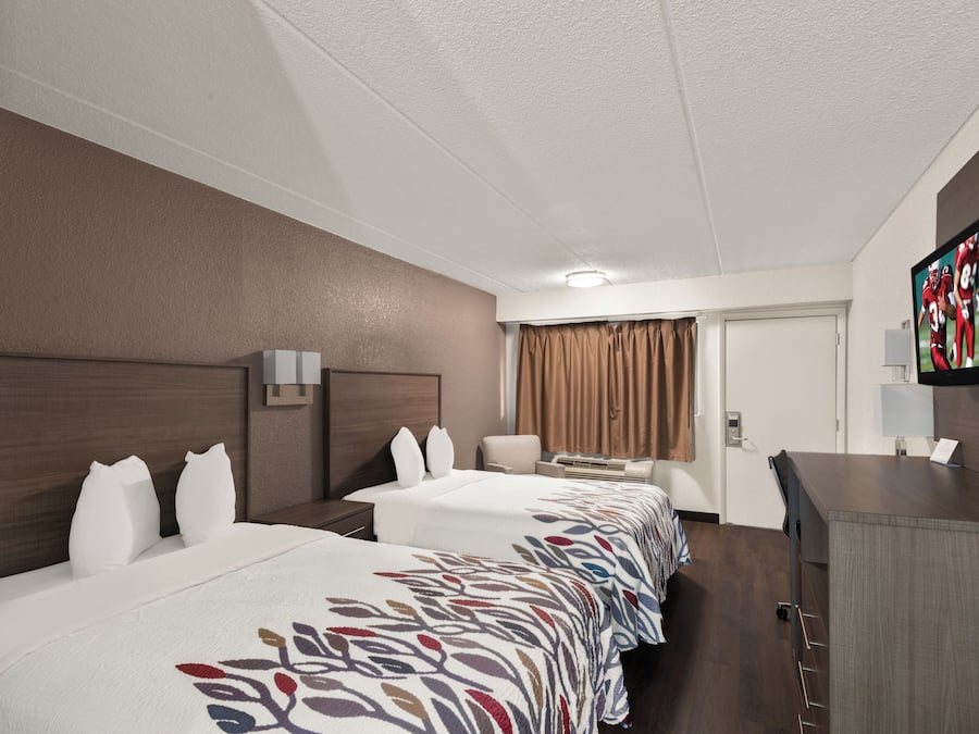 Quarto de hotel com duas camas, uma mesa de trabalho, uma televisão e uma porta.