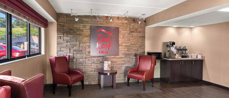 Un hall d’hôtel avec un mur en pierre, deux fauteuils en cuir rouge, un appareil à café et une enseigne indiquant « Red Roof Inn ».