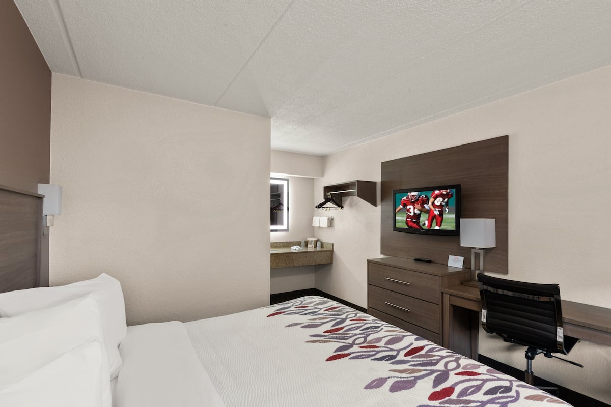 Een hotelkamer met een bed, een bureau met stoel, een televisie en een badkamer in de achtergrond.
