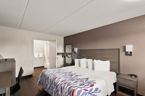 A hotel room with a bed, bedside table, and a desk with a chair.