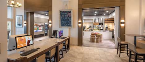 A hotel lobby with a reception desk, seating area, and a view into the kitchen.