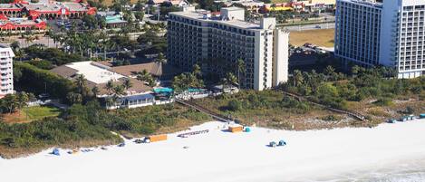 A coastal hotel with multiple high-rise buildings, a beach with umbrellas, and a clear view of the ocean.