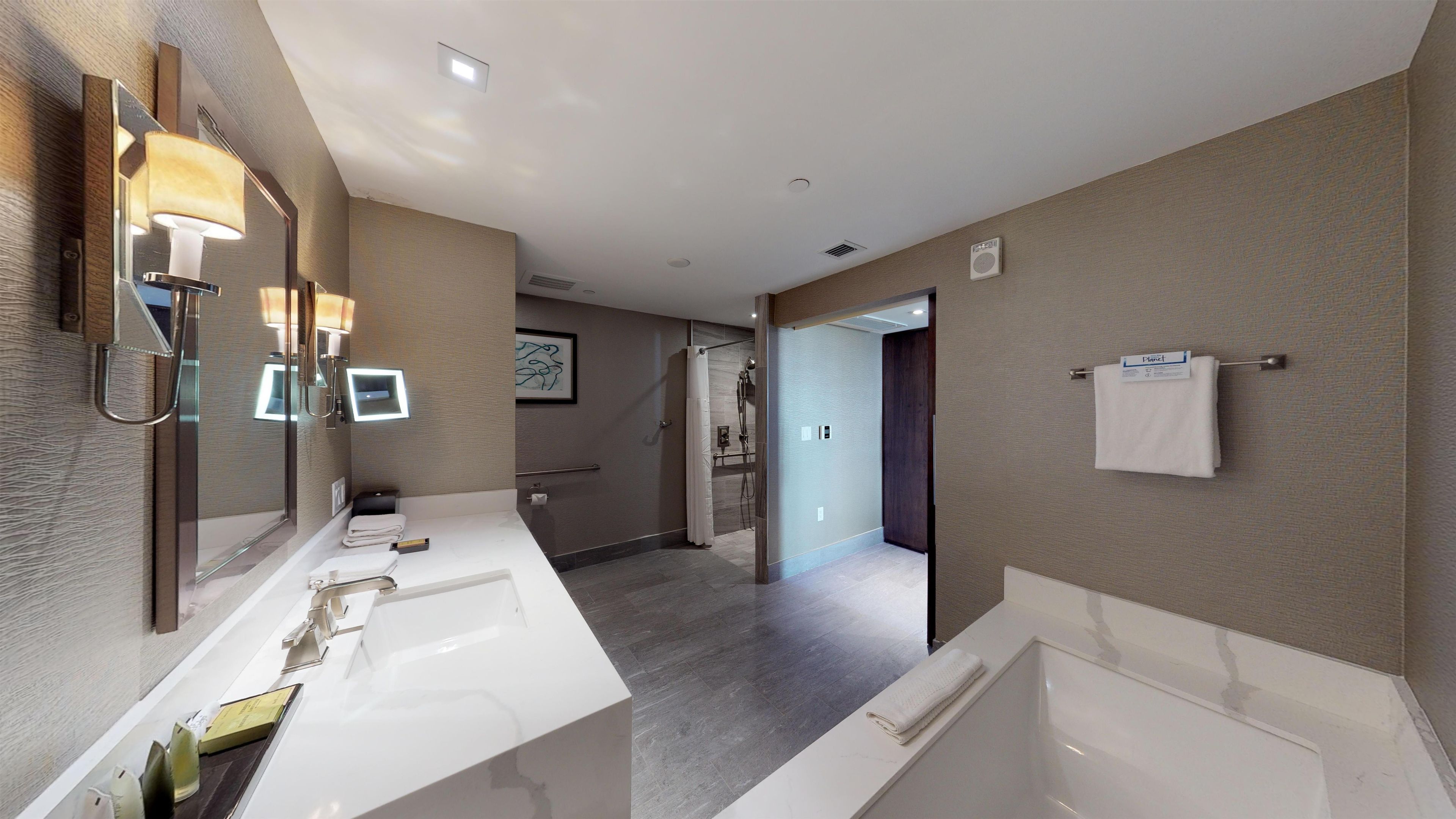 A modern bathroom with a large mirror, two sinks, a bathtub, and a shower area.