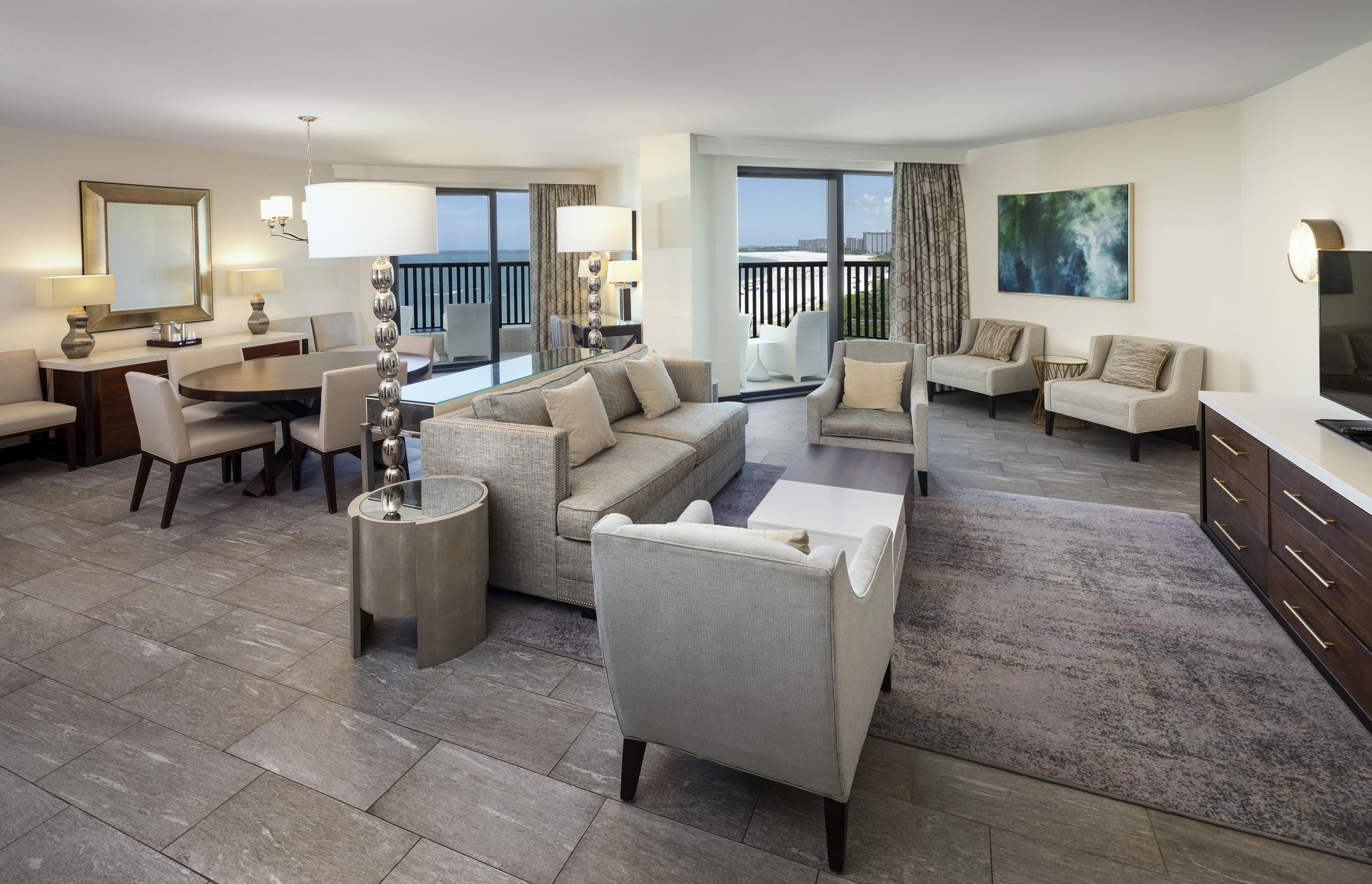 Una habitación de hotel moderna con zona de estar, comedor y balcón con vistas.