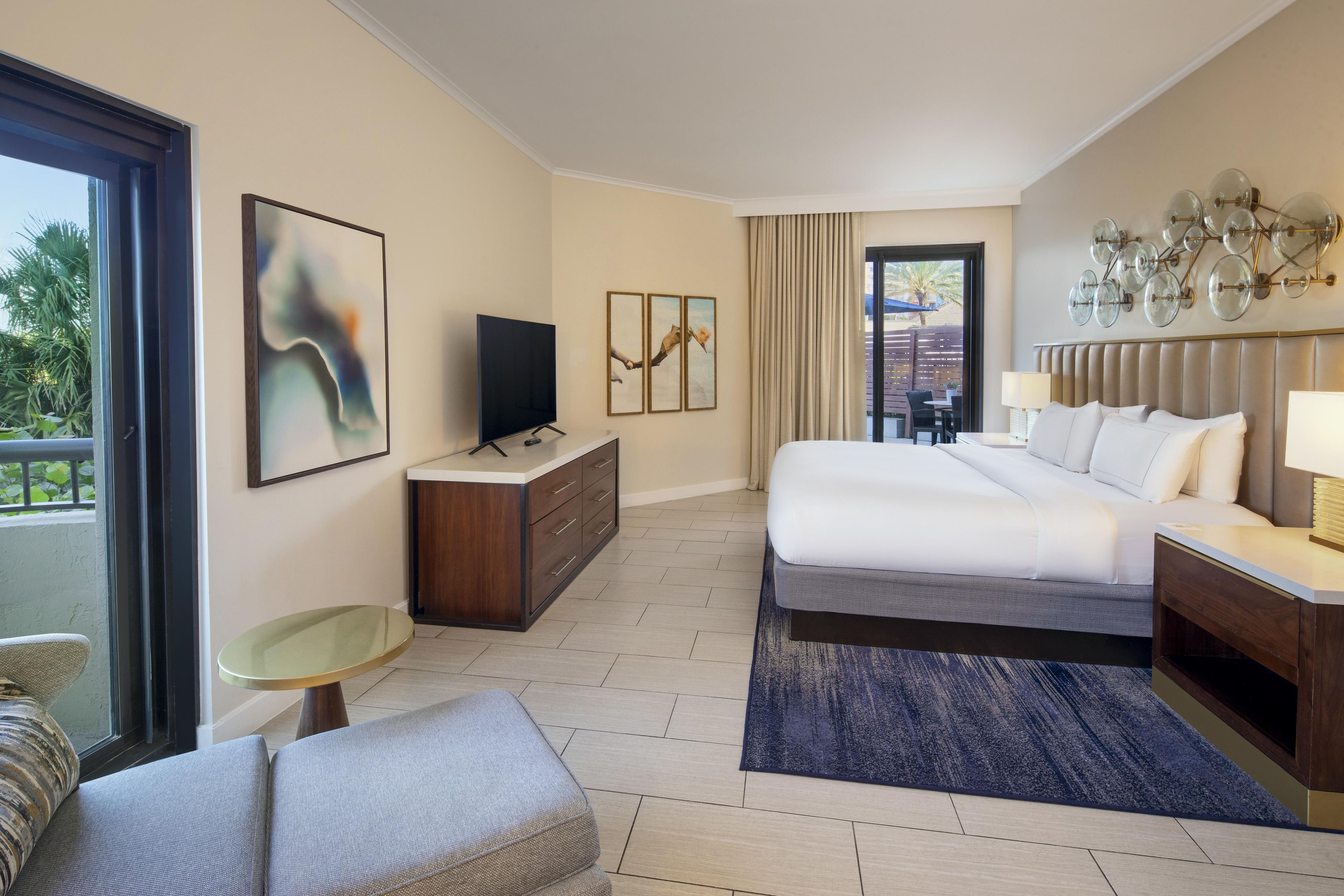 A hotel room with a bed, a TV, a desk, a chair, a balcony view, and a dining area.