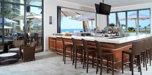 A bar area with a view of the ocean, wicker furniture, and a bar counter with various bottles. - Hilton Marco Island Beach Resort and Spa (Marco Island)