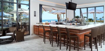 Zona de bar con vista al océano, muebles de mimbre y barra con diferentes botellas.