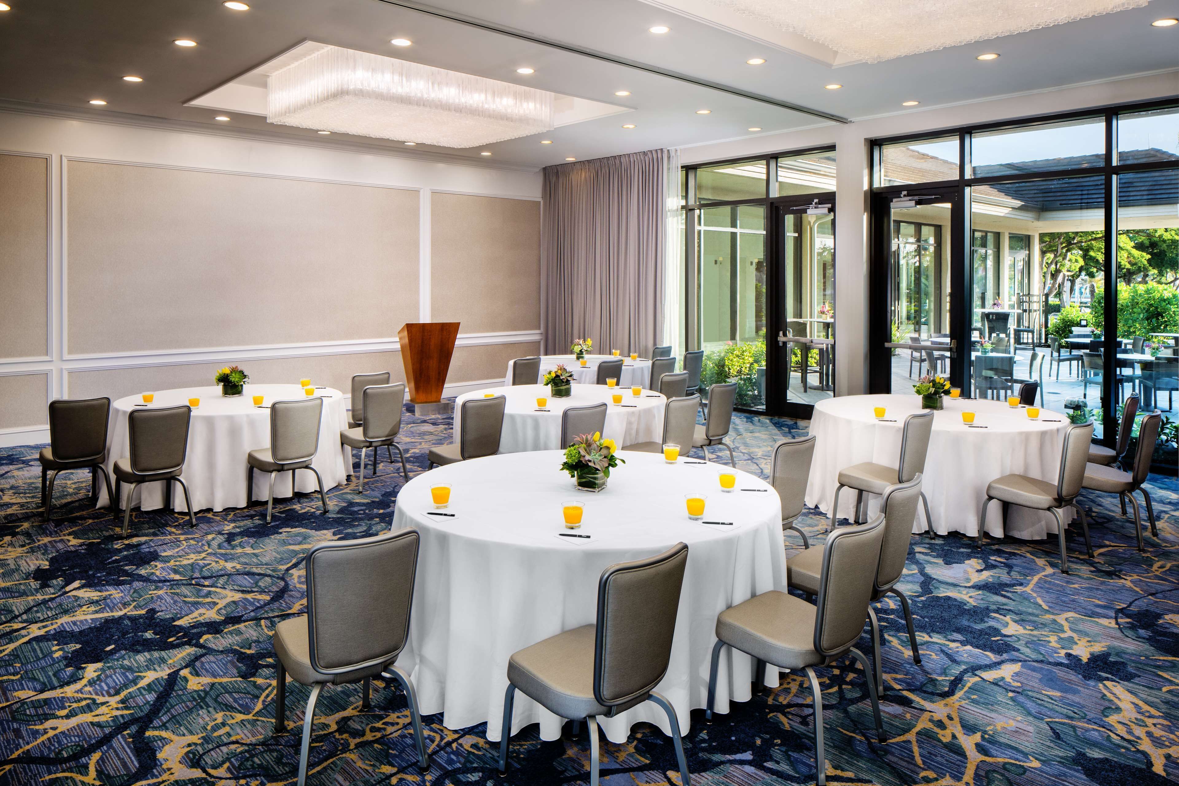 Une salle de conférence dotée de plusieurs tables rondes, chacune entourée de chaises, et d’une grande fenêtre offrant une vue sur l’extérieur.