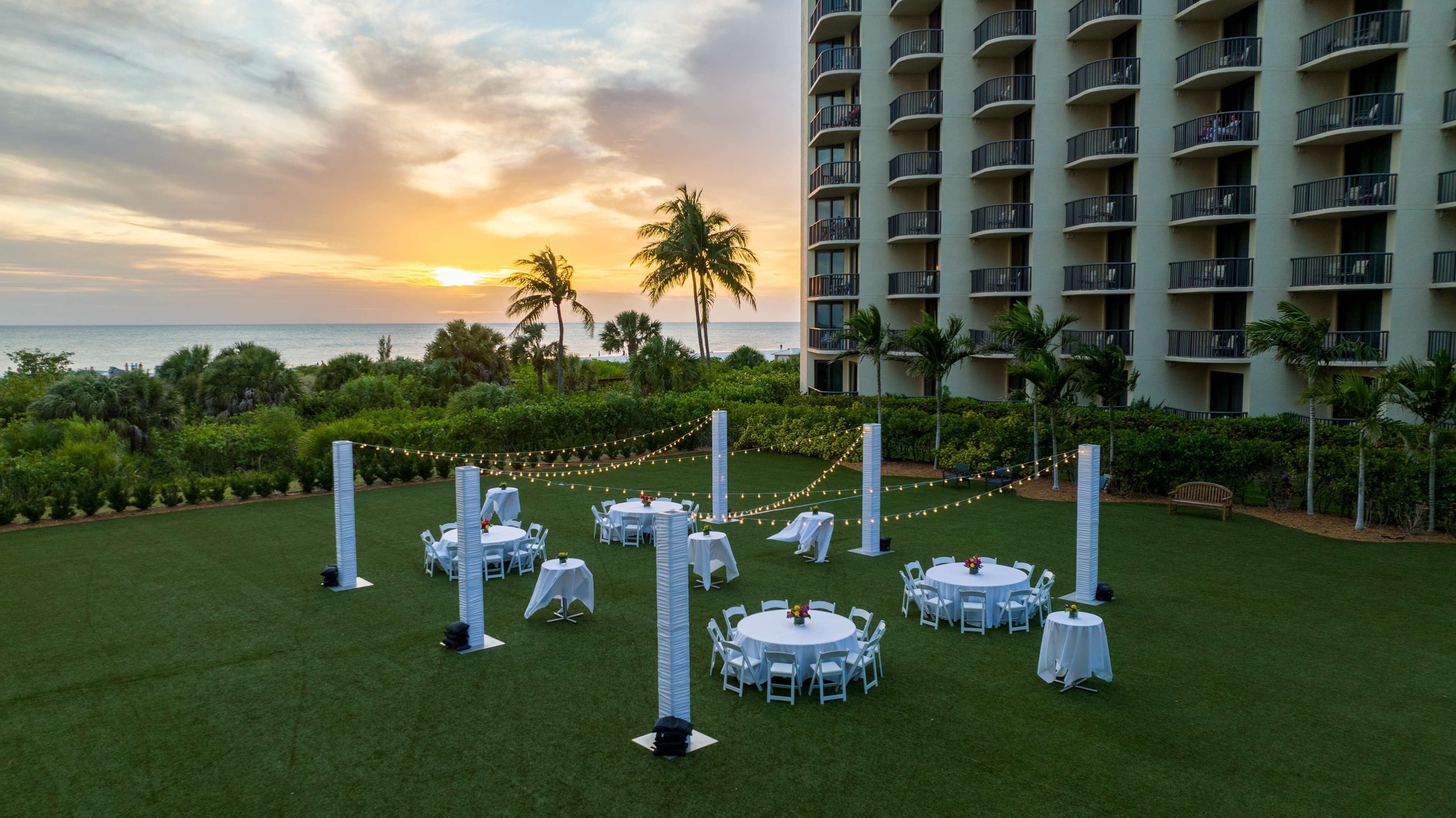 Un resort con zonas de comedor al aire libre, palmeras y vista al océano al atardecer.
