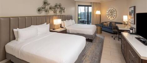 A hotel room with two beds, a desk, a TV, and a balcony with a view.