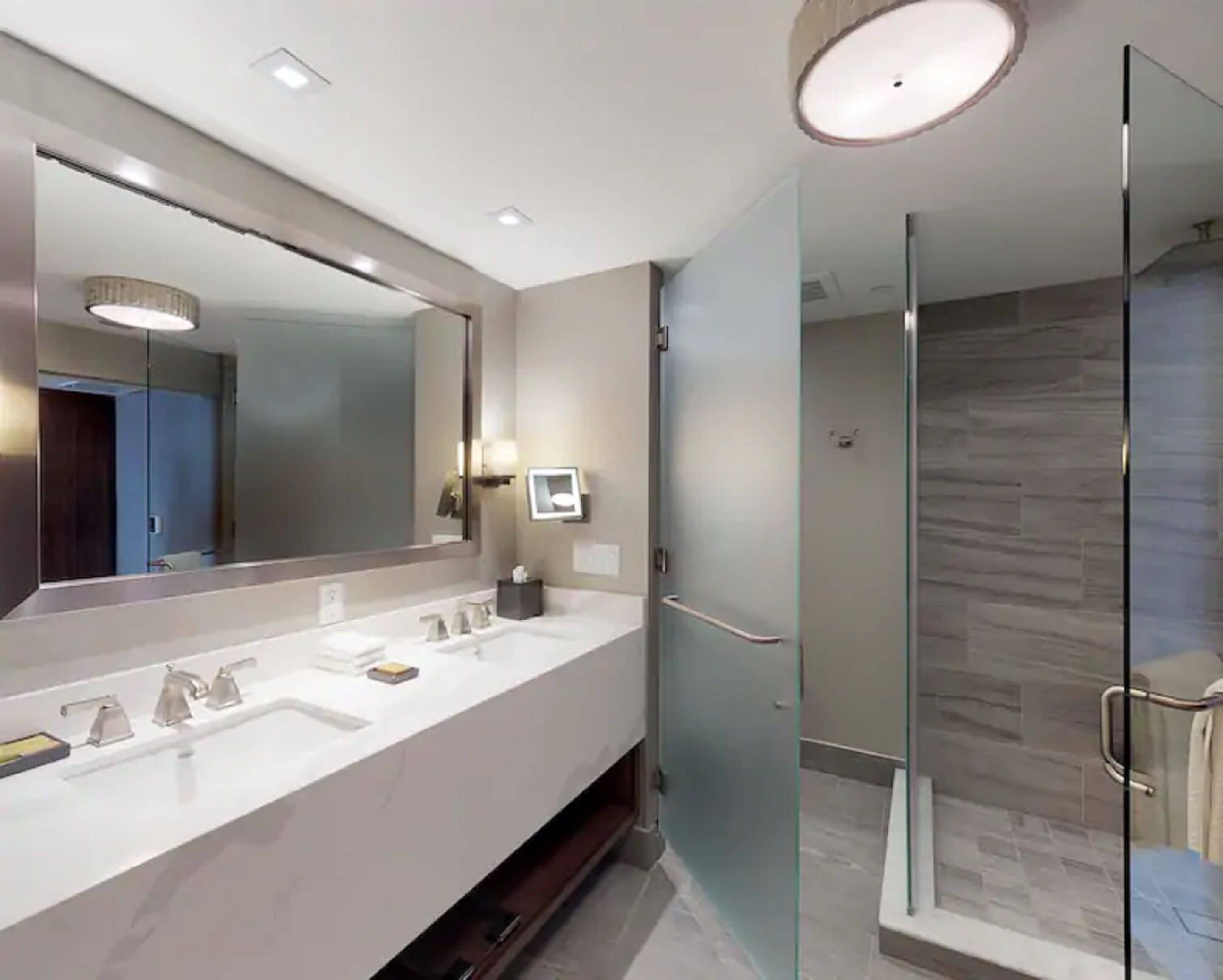 Un bagno moderno con un ampio specchio, un mobile lavabo bianco e una cabina doccia in vetro.