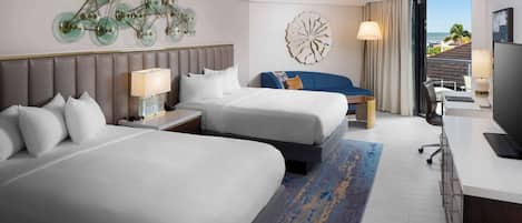 A hotel room with two beds, a desk, a TV, and a view of the beach.