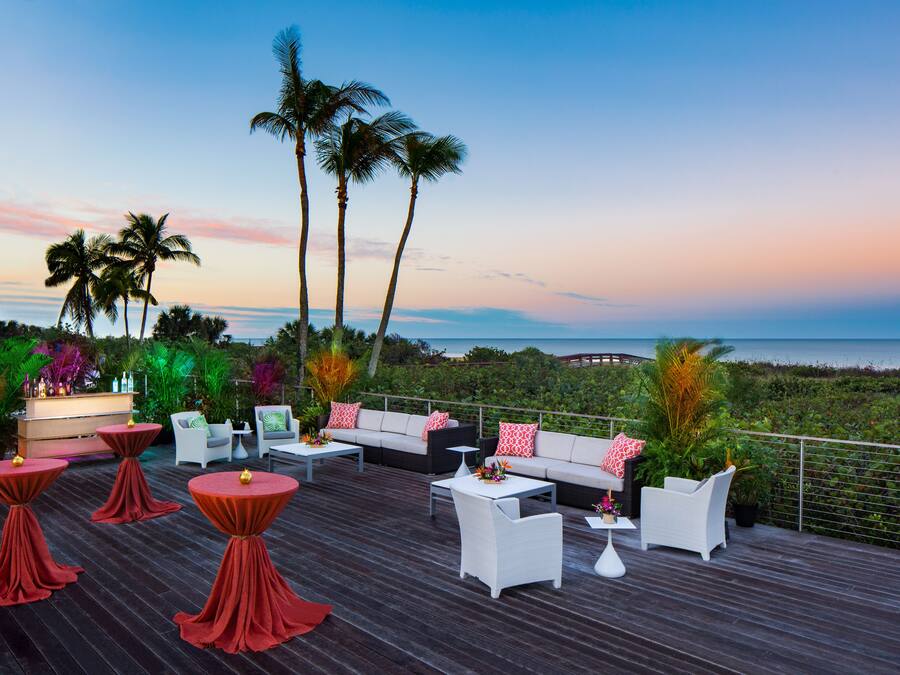 Terraza con mobiliario exterior, palmeras y vista al océano.