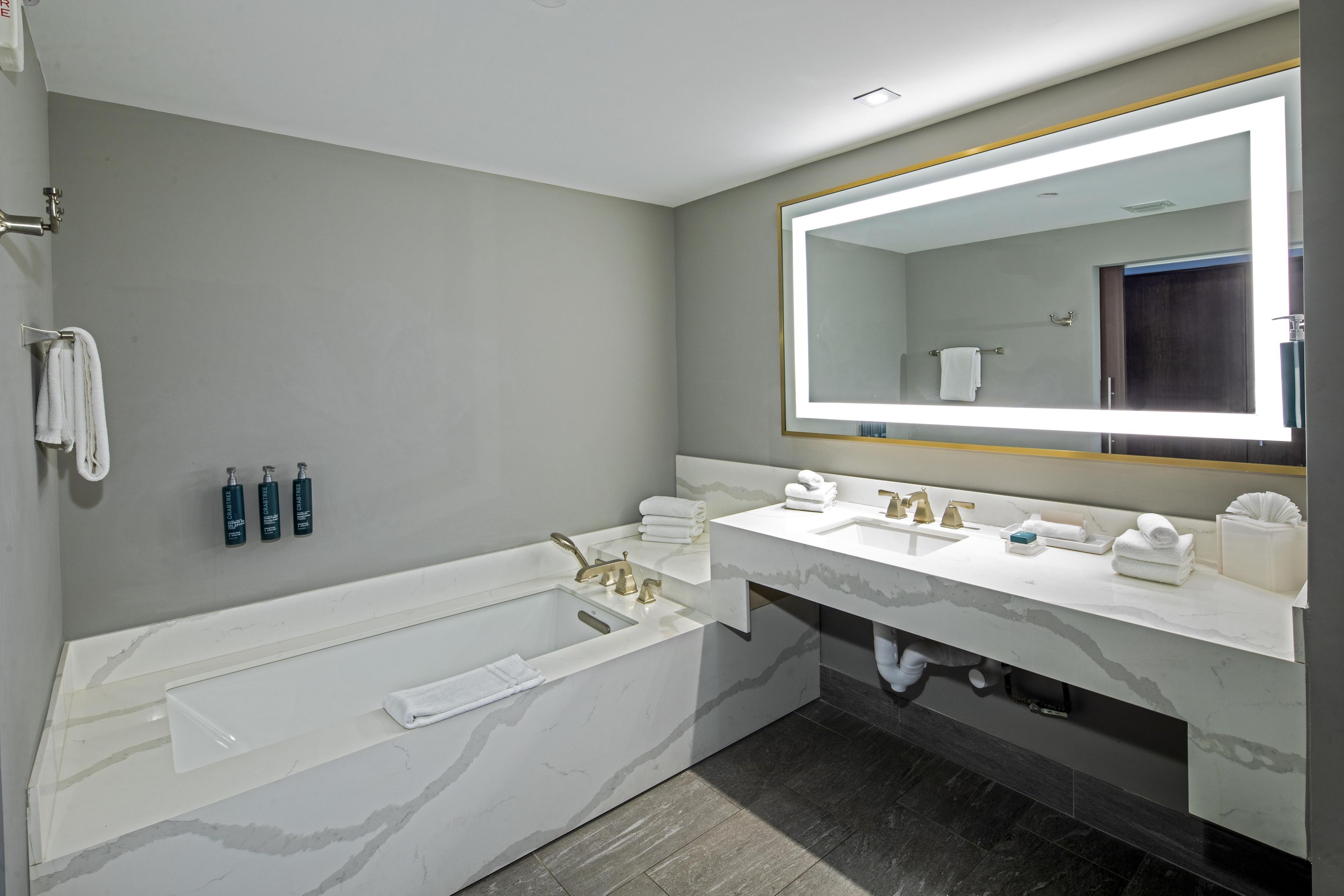 A modern bathroom with a bathtub, two sinks, and a large mirror.