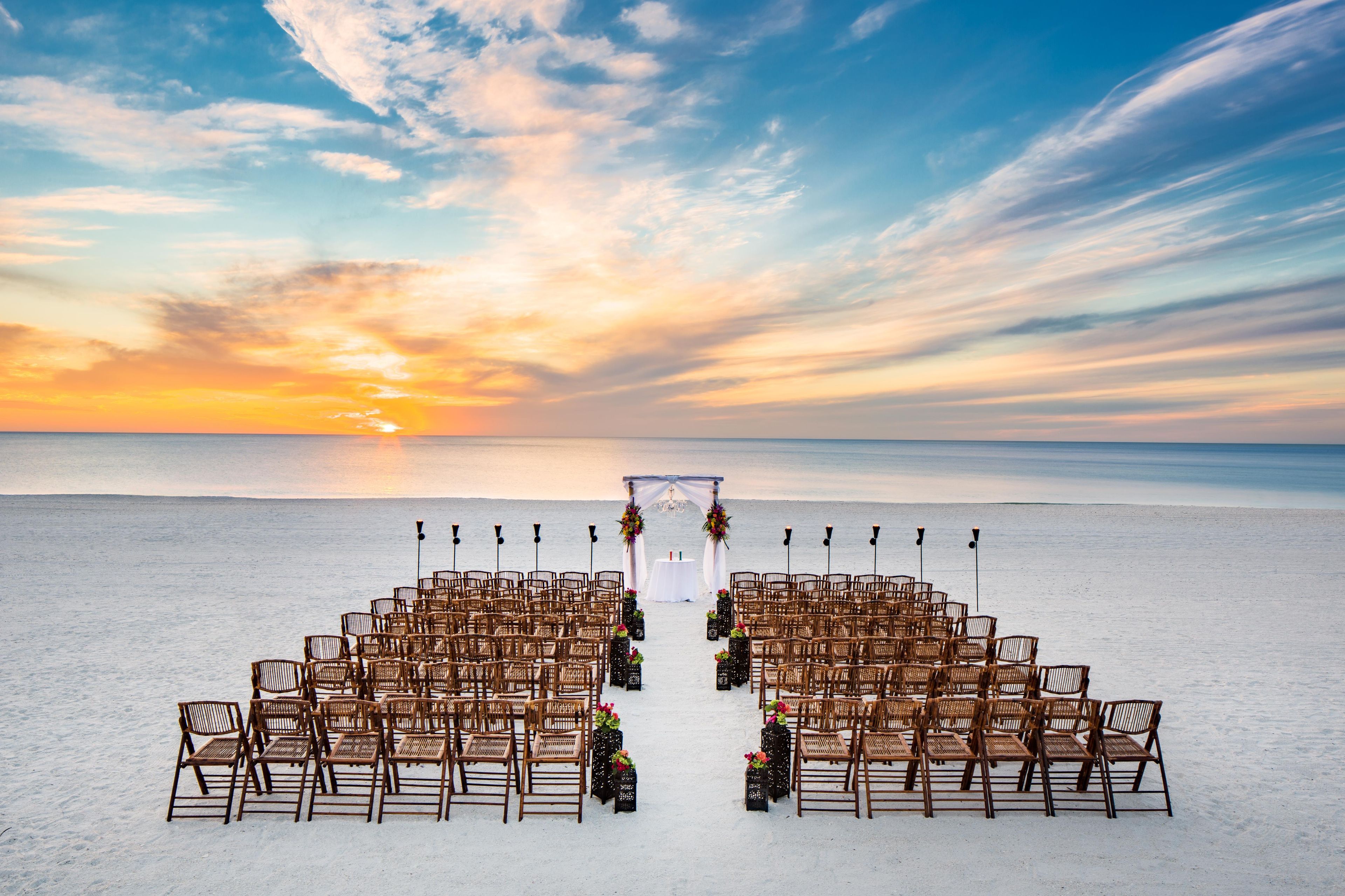 Een strandbruiloft setting met rijen stoelen en een witte boog.