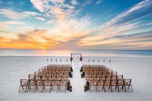A beach wedding setup with rows of chairs and a white archway.