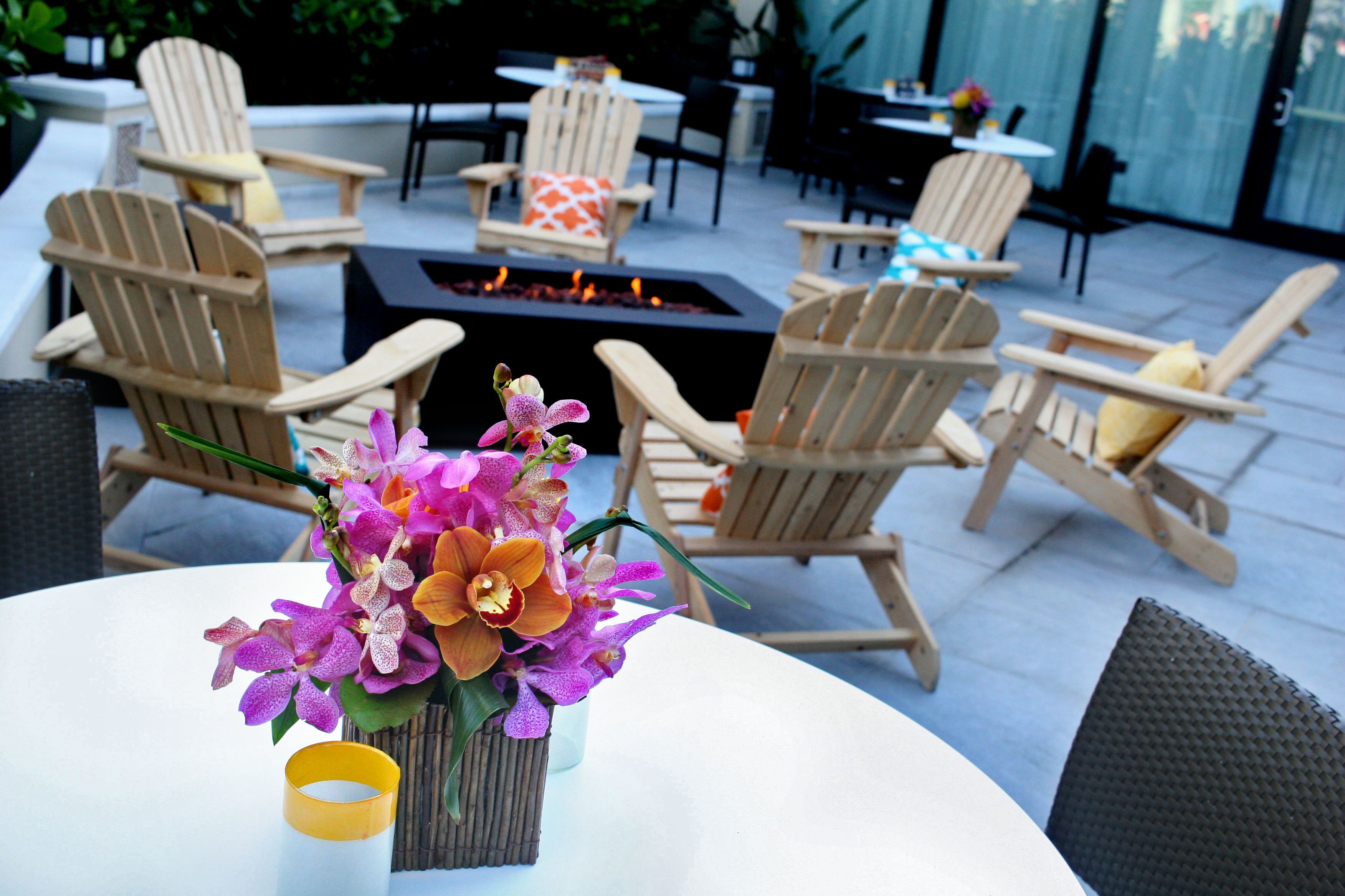 Un espace patio aménagé avec des fauteuils Adirondack, une table ronde ornée d’un vase de fleurs et un foyer extérieur.