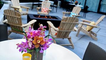 Un espace patio aménagé avec des fauteuils Adirondack, une table ronde ornée d’un vase de fleurs et un foyer extérieur.