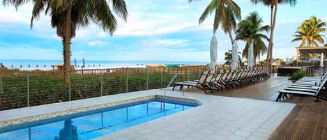 A pool area with lounge chairs and a view of the beach.