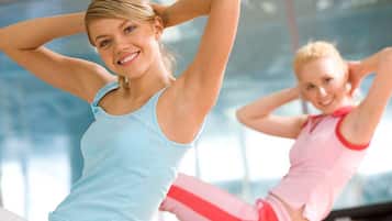 Two individuals in a gym setting, one in a light blue tank top and the other in a pink top, stretching.