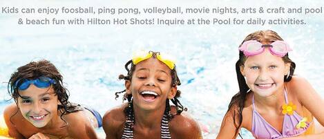 A promotional poster for Hilton Hot Shots featuring children in a pool, highlighting activities like foosball, ping pong, volleyball, movie nights, arts & crafts, and pool & beach fun.