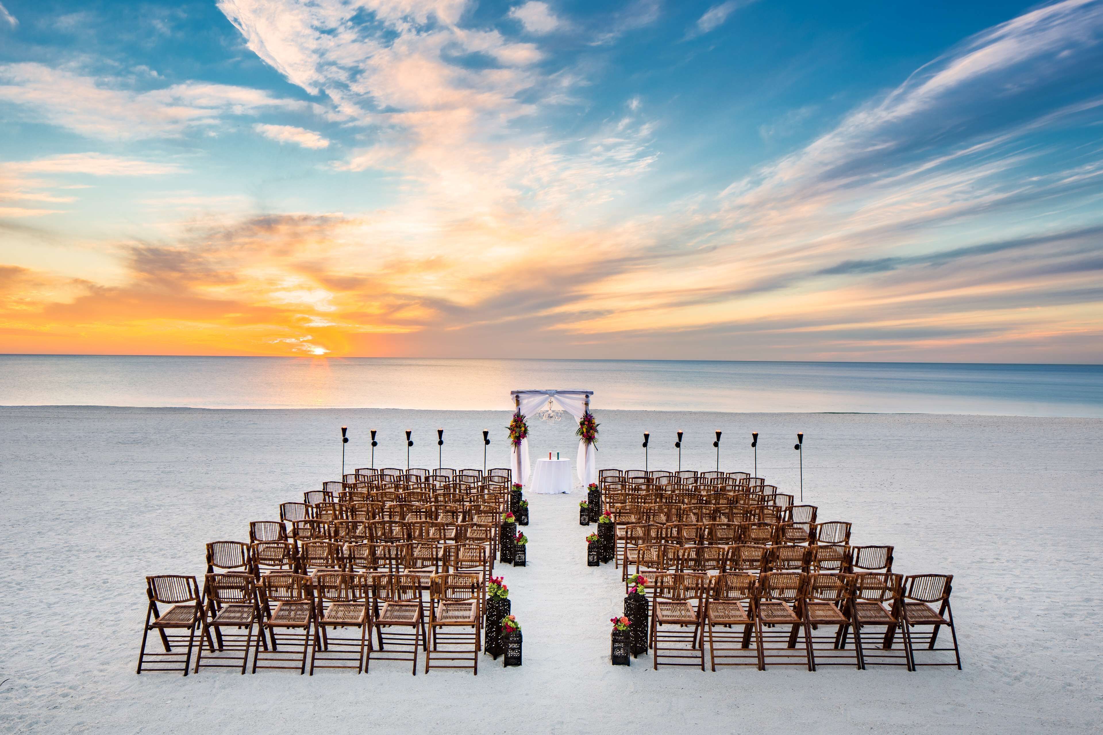 Een strandbruiloft decoratie met rijen stoelen en een middenpad dat leidt naar een witte boog.