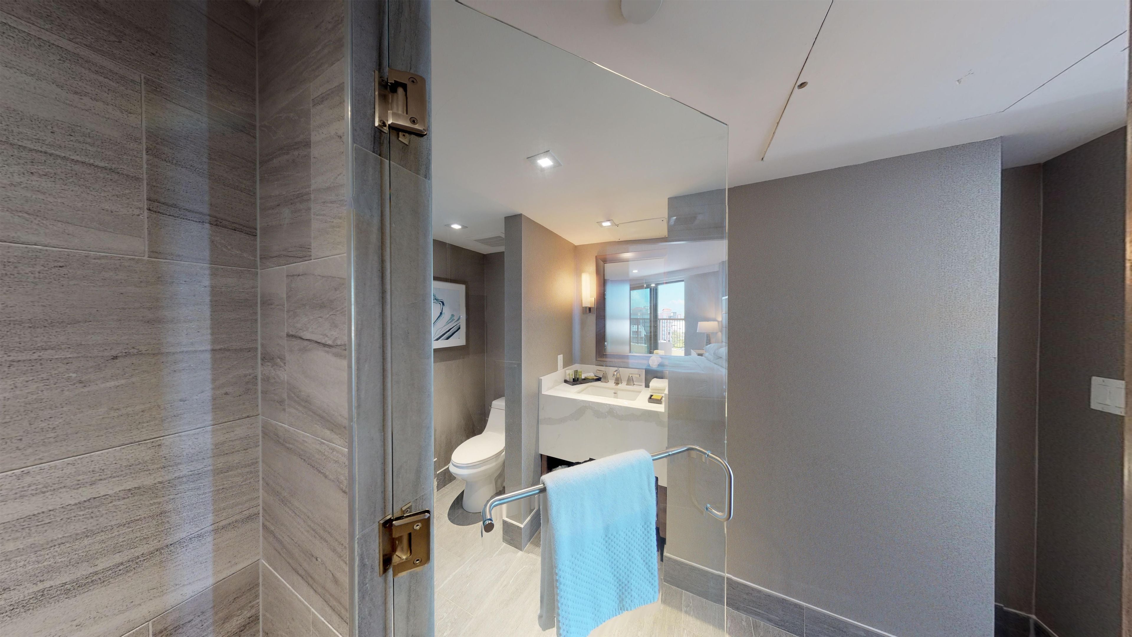 A modern bathroom with a glass shower enclosure, a toilet, and a sink with a towel rack.