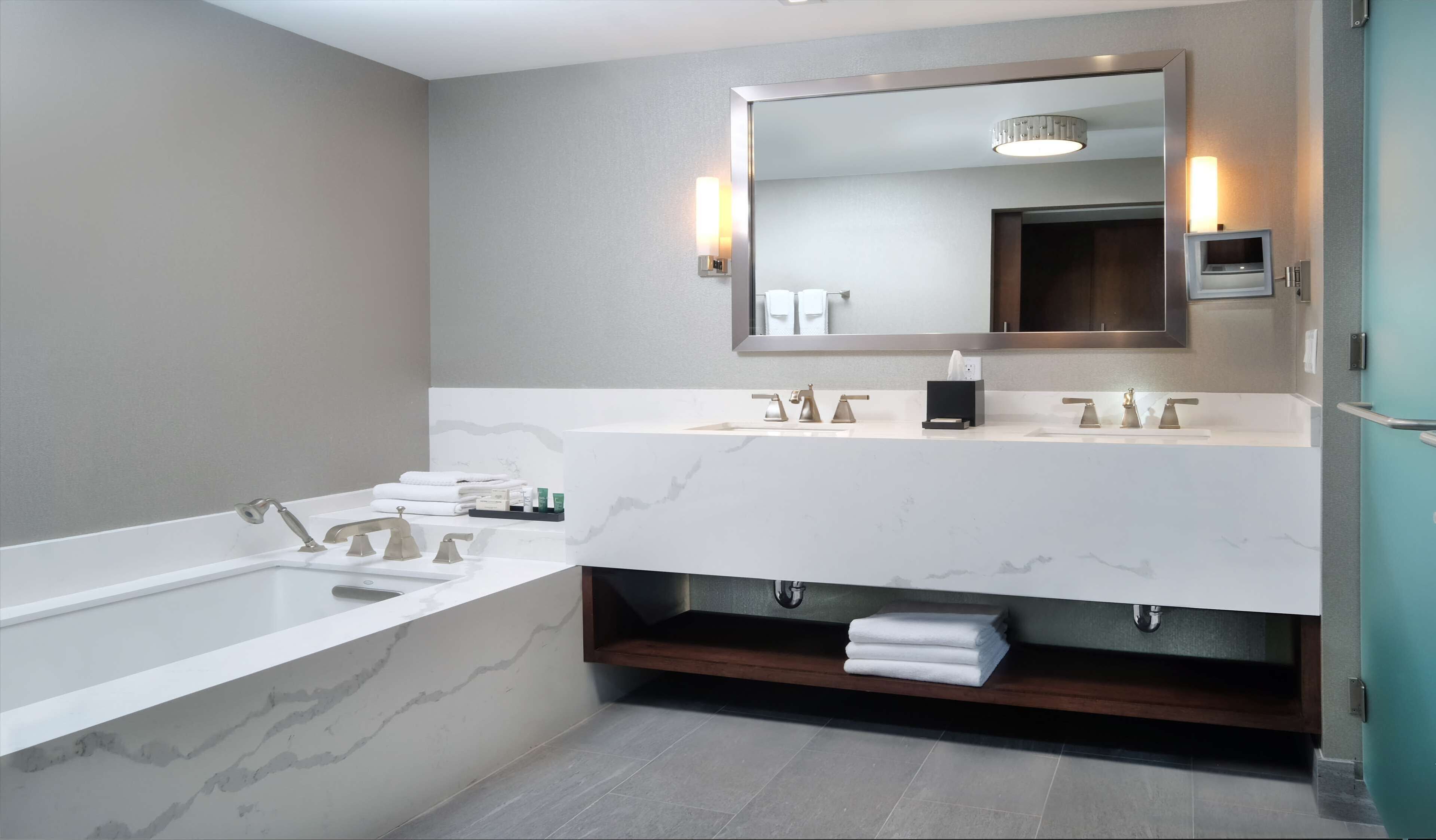 A modern bathroom with a large bathtub, two sinks, and a mirror above.