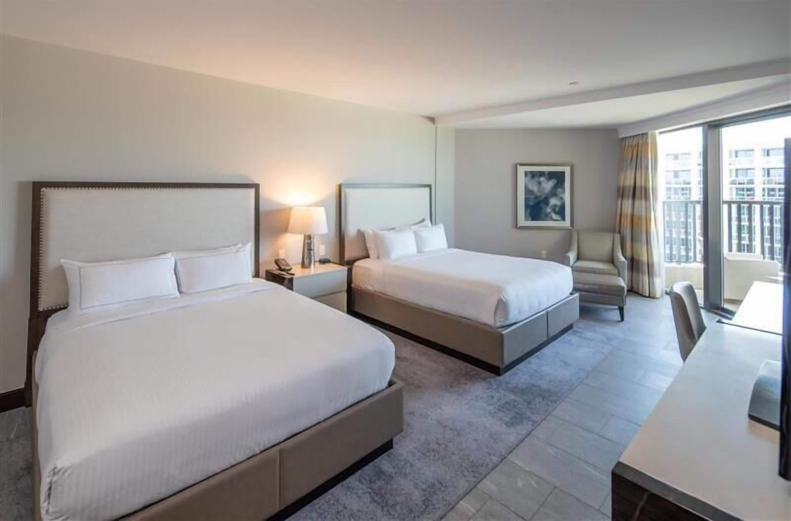 A hotel room with two beds, a desk, and a large window with a view.
