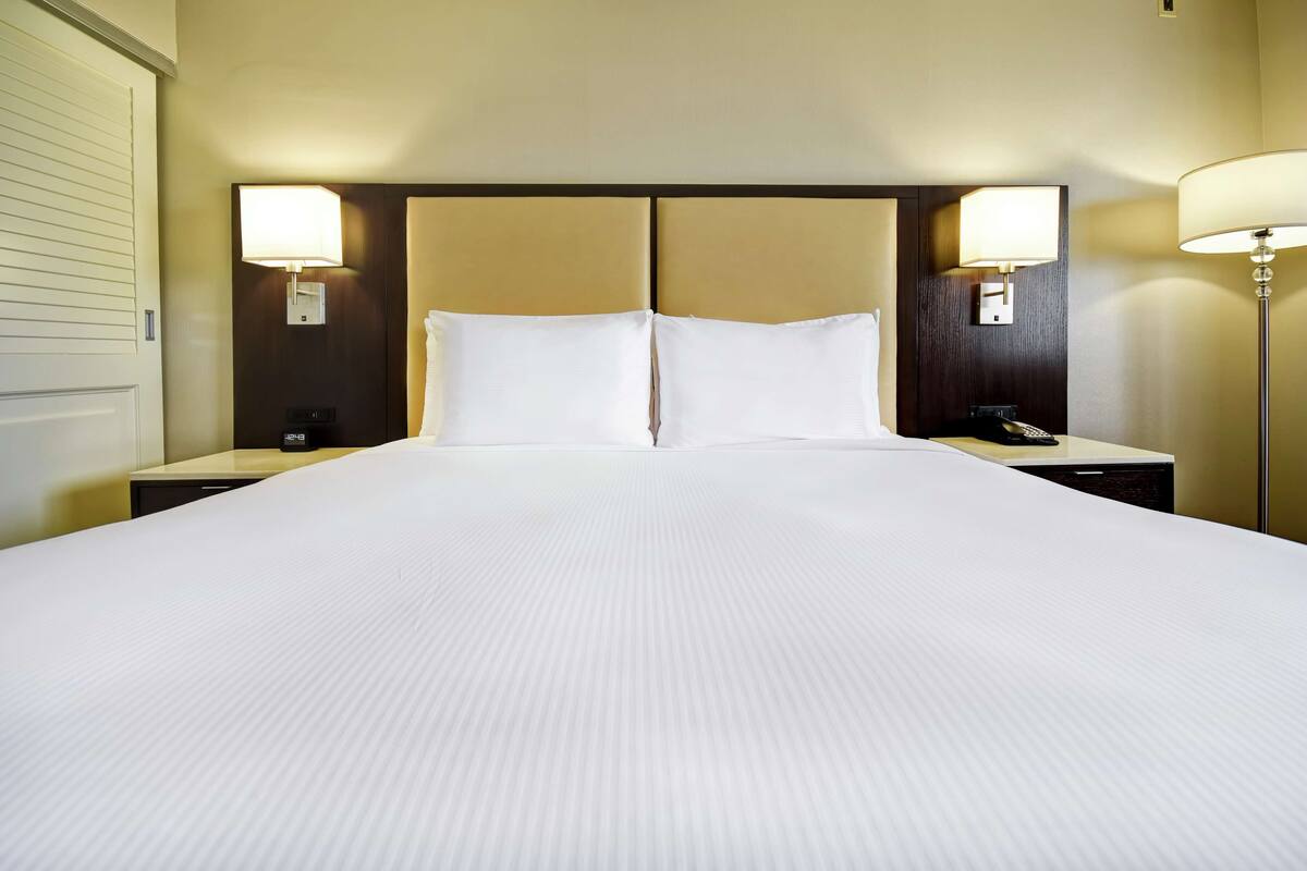 A hotel room with a large bed, two bedside tables, and two wall-mounted lamps.