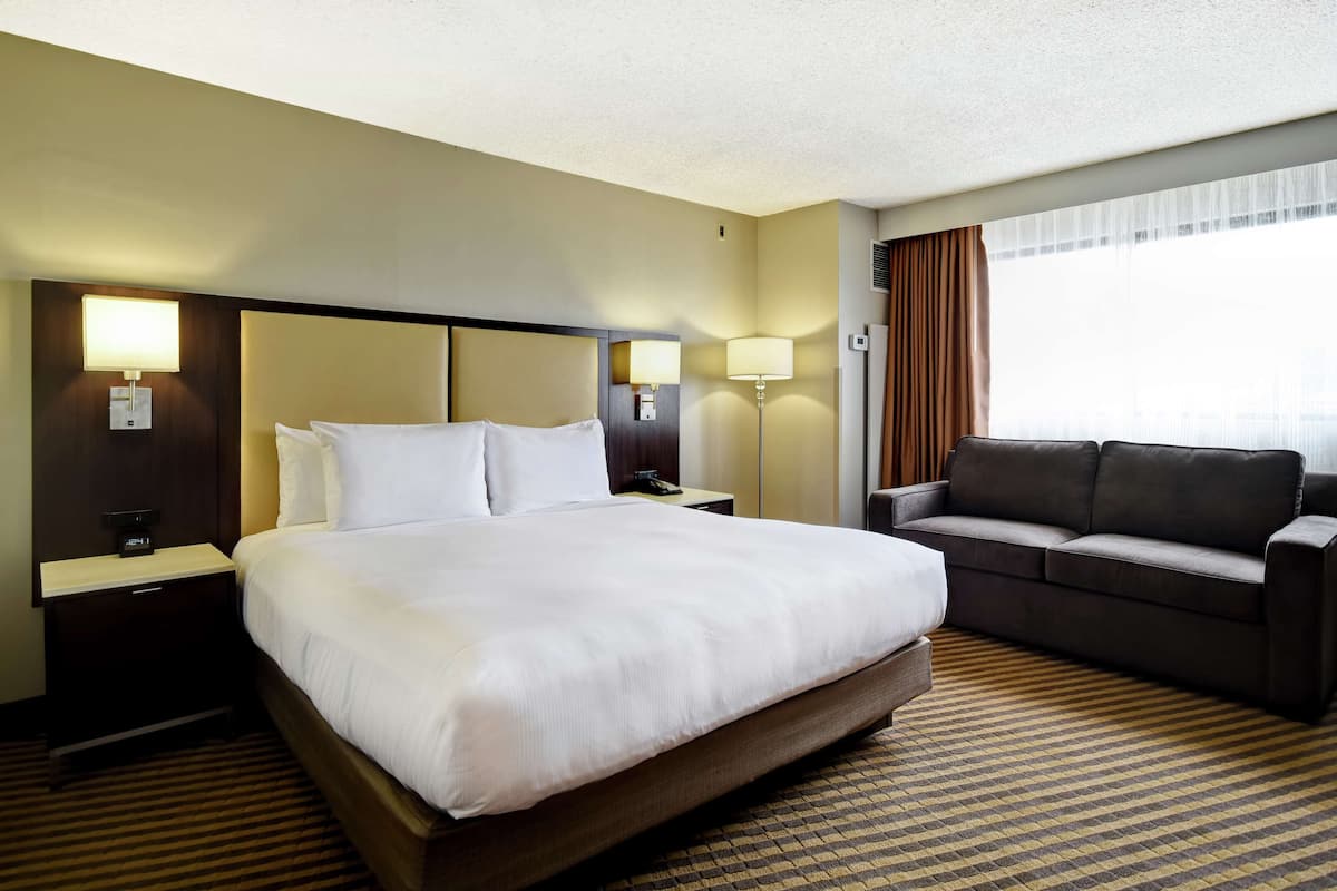 A hotel room with a large bed, a sofa, two bedside lamps, and a window with curtains.