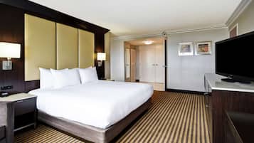 Quarto de hotel com uma cama grande, televisão, escrivaninha com luminária e armário.