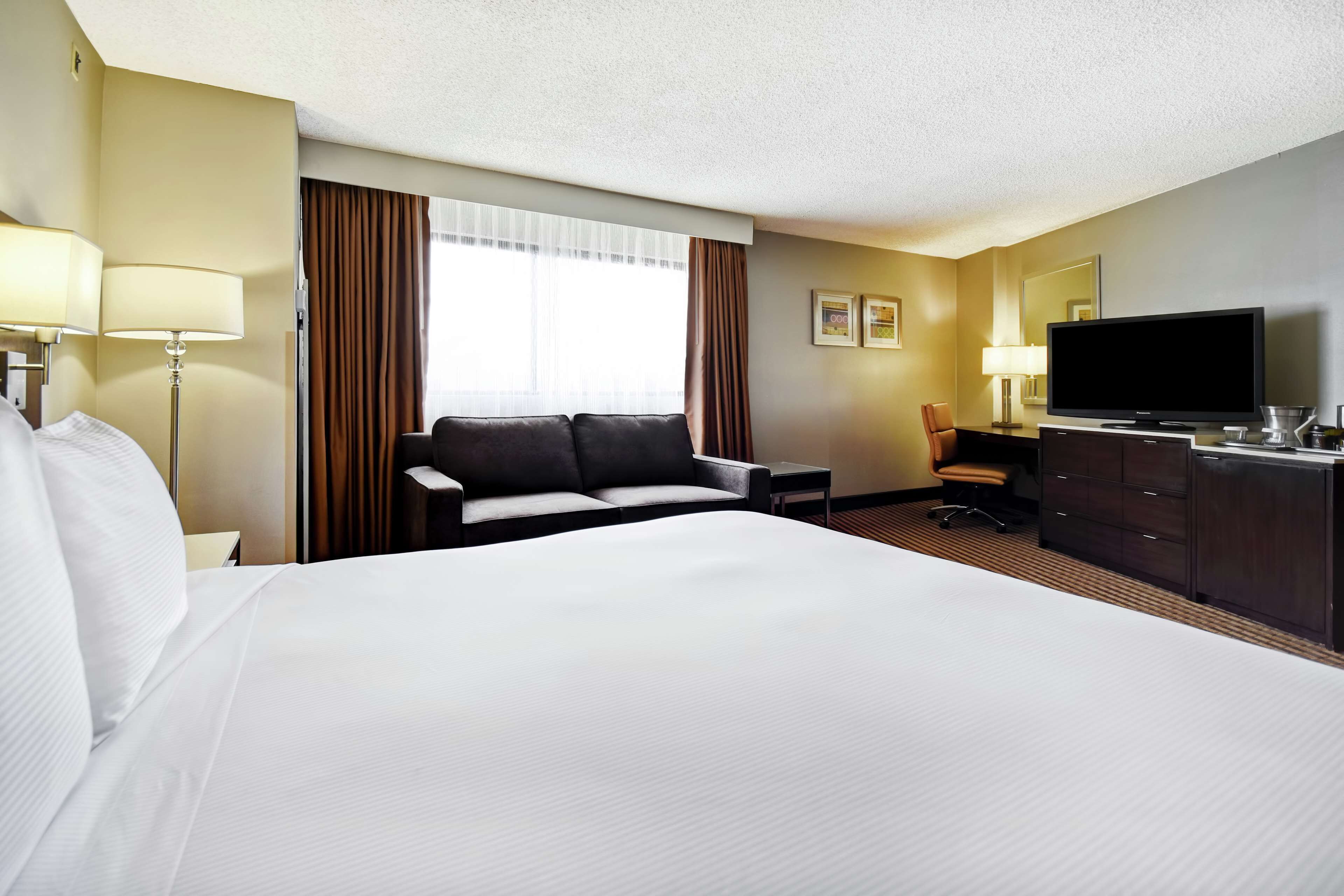 A hotel room with a large bed, a sofa, a desk with a television, and a dresser.