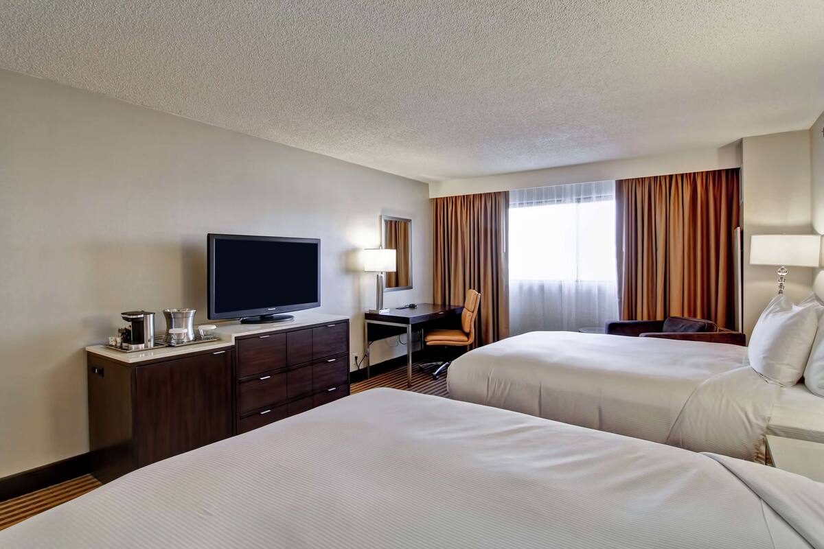 A hotel room with two beds, a desk with a television, a coffee maker, and a lamp.