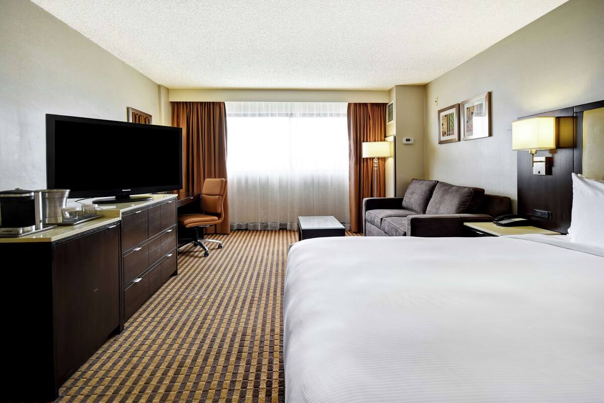 A hotel room with a large bed, a flat-screen TV, a desk with a lamp, a chair, and a sofa.