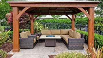 A covered outdoor seating area with a wooden pergola, cushioned sofas, and a central coffee table.