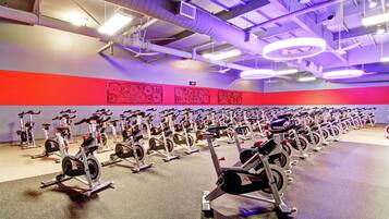 Un gimnasio con hileras de bicicletas estáticas, una pared roja con diseño circular e iluminación colgante.