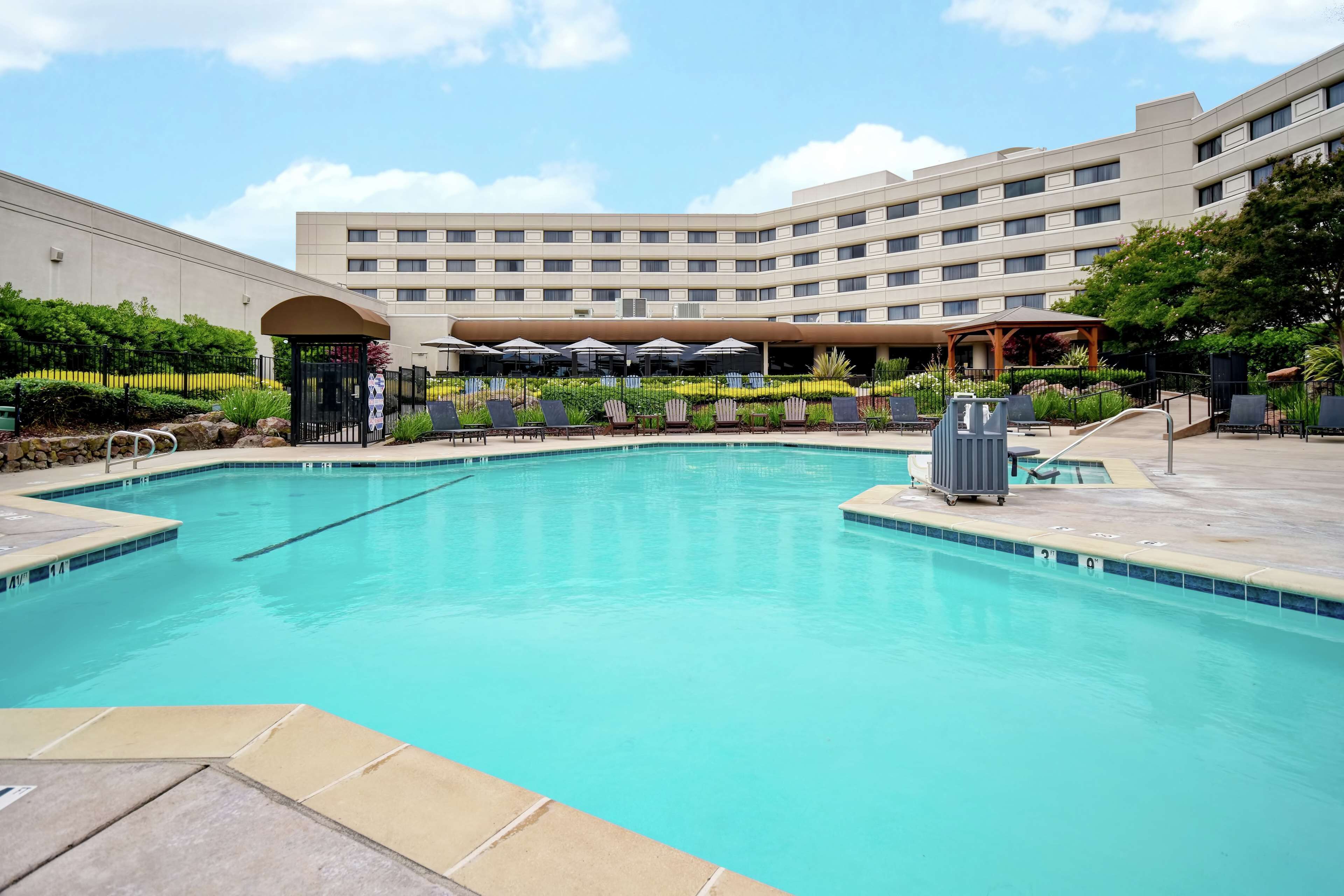 A swimming pool with lounge chairs and umbrellas, surrounded by a landscaped garden and a hotel building.