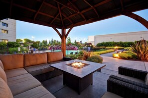 Un patio al aire libre con un brasero, una zona de estar y vistas a una piscina y follaje.