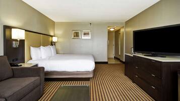 Quarto de hotel com cama, televisão, escrivaninha e sofá.