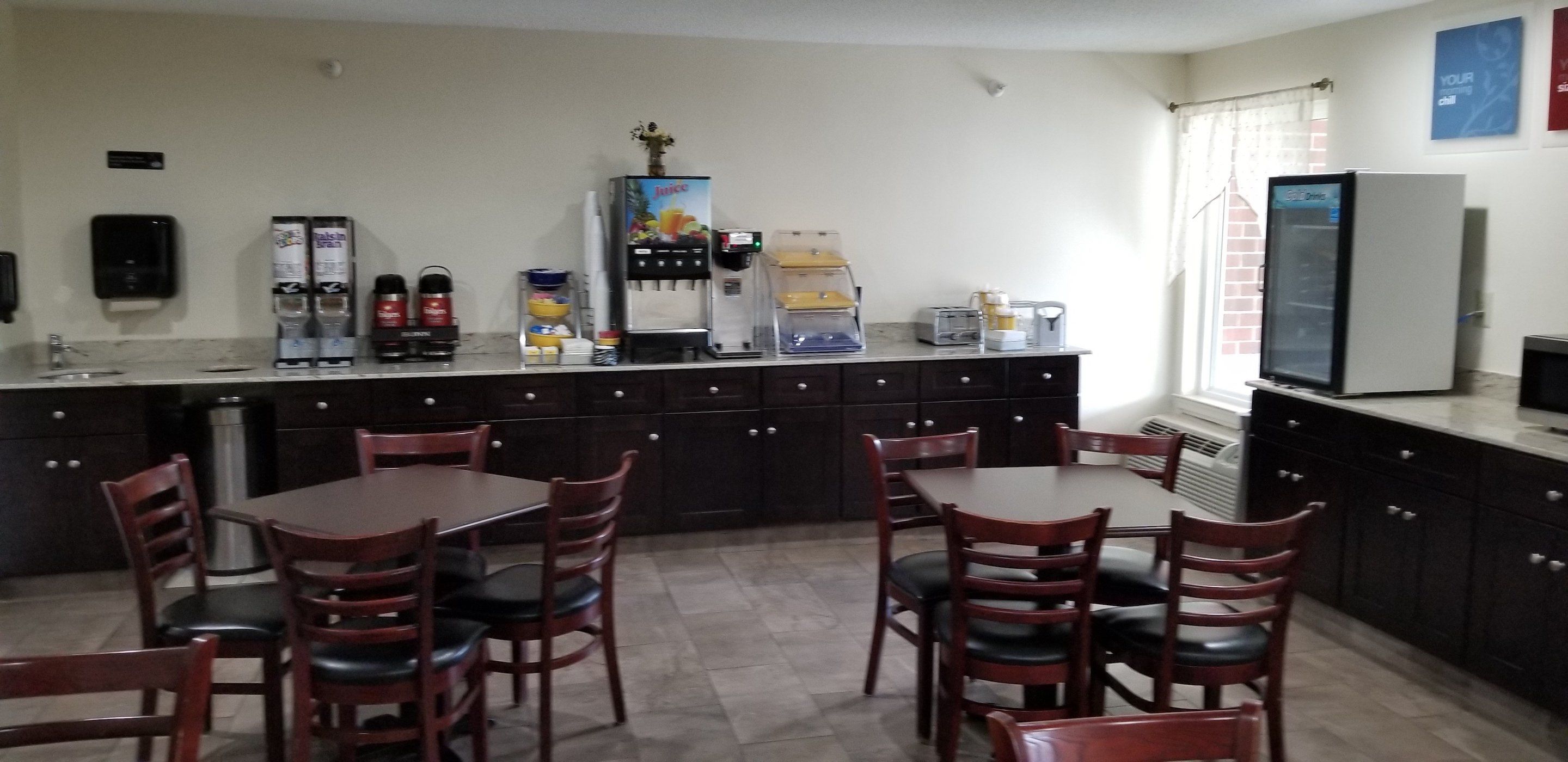 A compact kitchen with dark cabinets, a coffee machine, a juice dispenser, and a refrigerator.