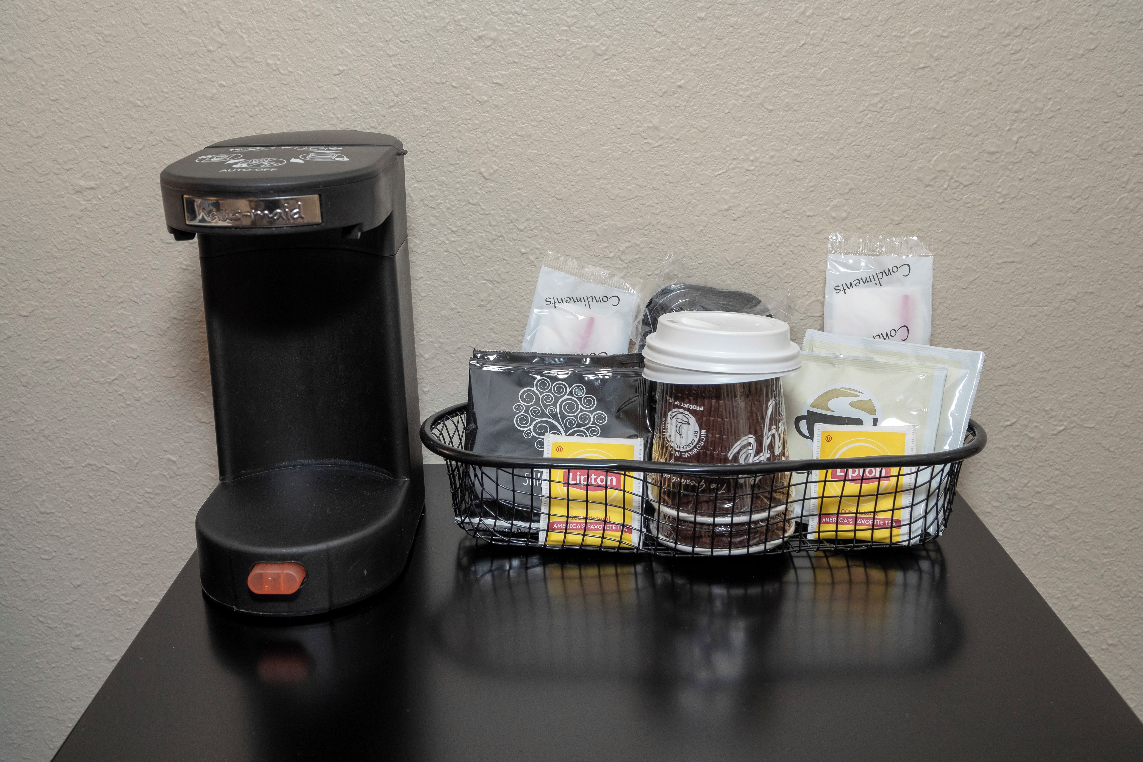 Una cafetera, una cesta con cápsulas de café y una taza sobre una mesa.